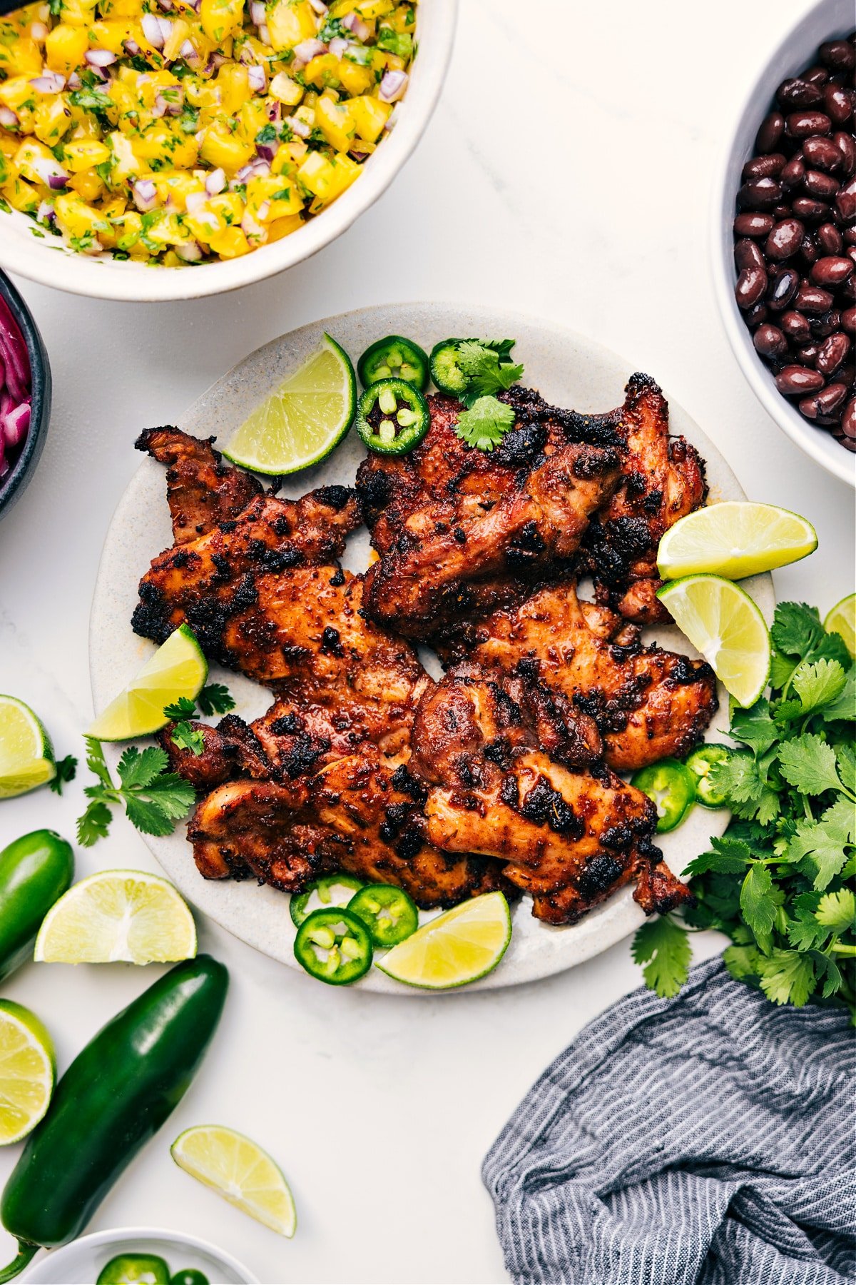 The Most Flavorful Jerk Chicken Recipe Plate of Jerk Chicken with fresh limes, jalapeños, and cilantro garnish.