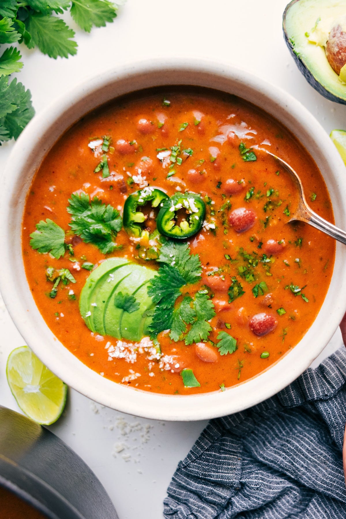 Pinto Bean Soup, or as we like to call it, Refried Bean Soup! This recipe is the perfect combination of quick, easy, healthy, and delicious. Not to mention, it's perfect for vegetarians and vegans! Recipe via ChelseasMessyApron.com #pintobeans #soup #pintos #vegetarian #vegan #quick #easy A bowl of this pinto bean soup recipe topped with fresh avocado, cilantro, and sliced jalapeños.