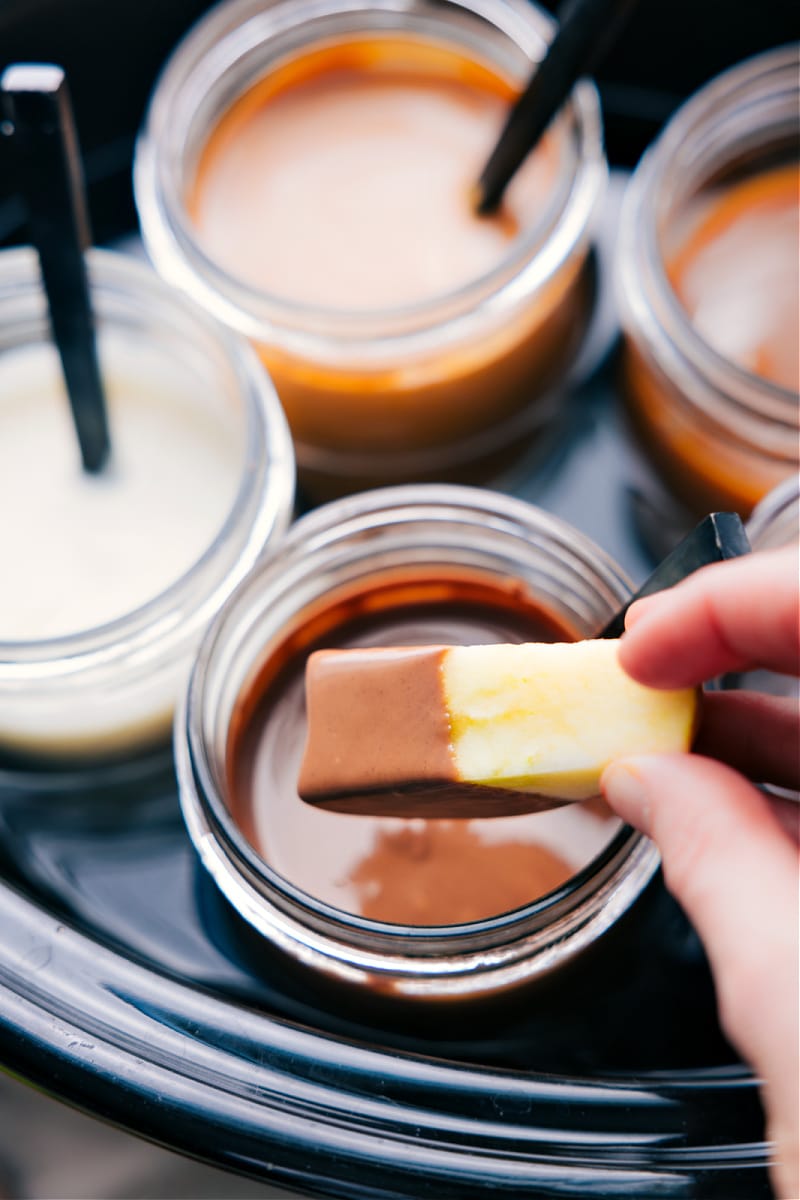 Overhead image of apples being dipped in the sauce with this caramel apple bar