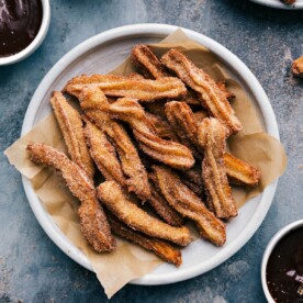 Plate of churros served with a side bowl of rich chocolate sauce.