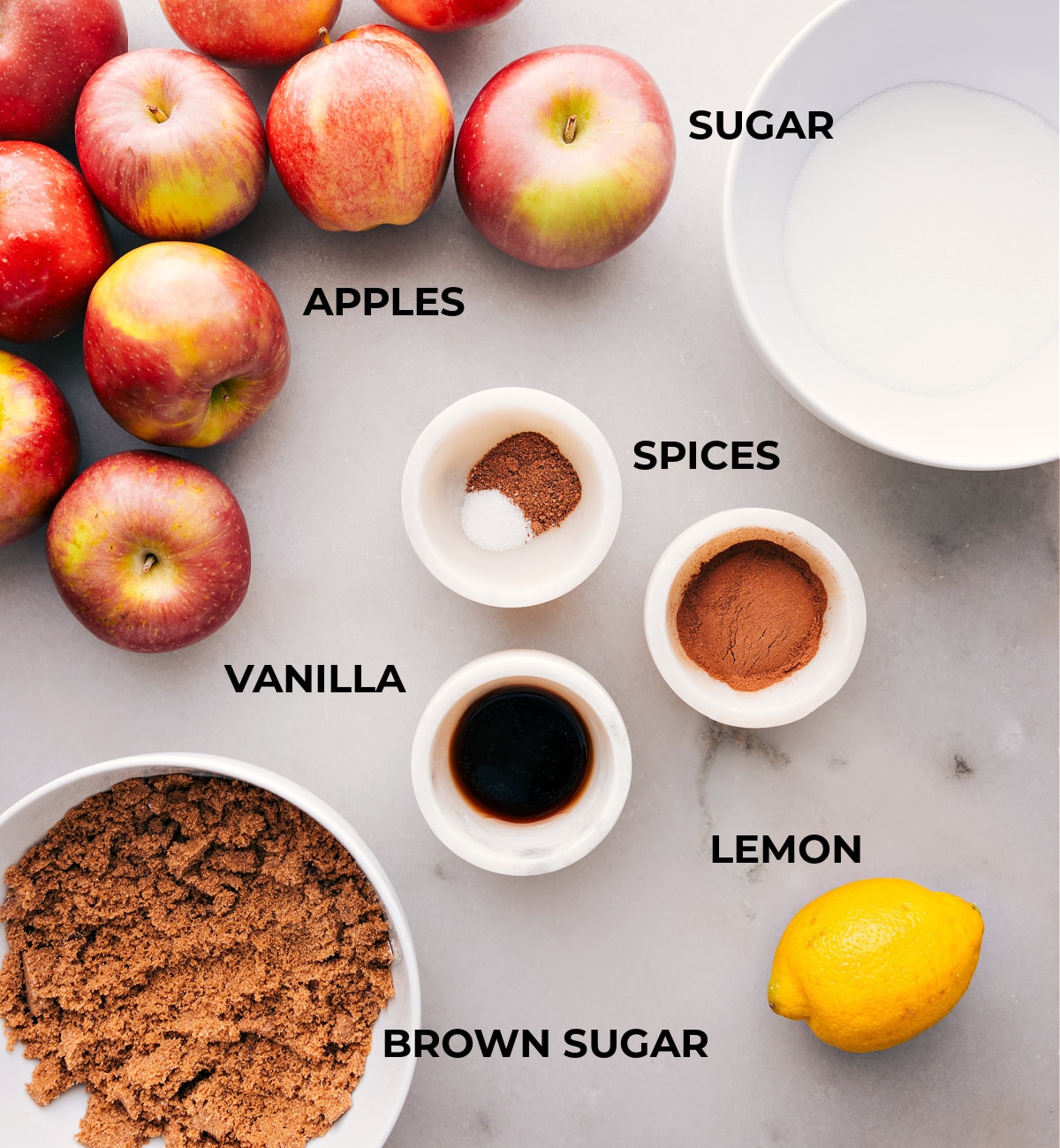 Assorted ingredients spread out, including fresh fruits, a mix of spices, vanilla extract, and granulated sugar.
