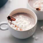 Finished steaming beverage in a mug, lavishly topped with whipped cream, marshmallows, and a cinnamon stick.