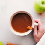 Hand holding a warm cup of apple cider with steam rising.