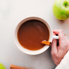 Hand holding a warm cup of apple cider with steam rising.