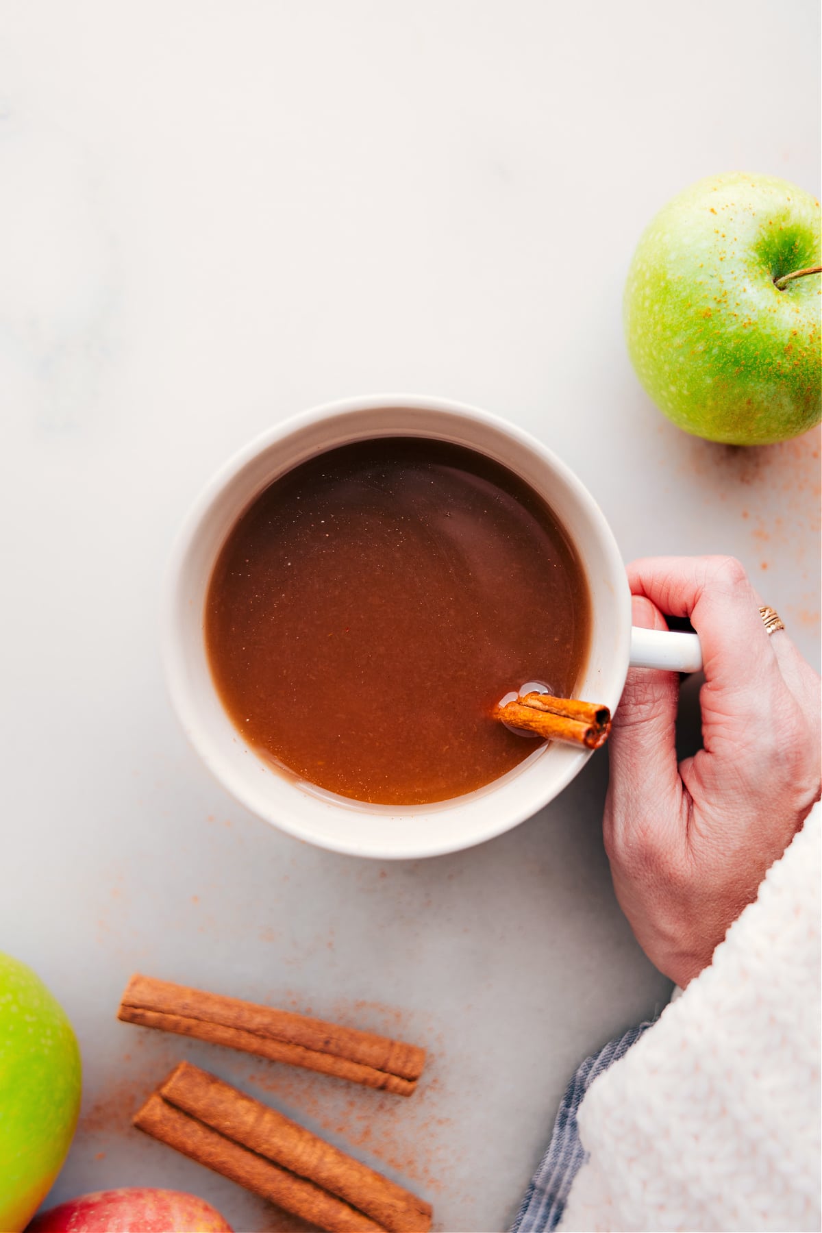 Hand holding a warm cup of apple cider with steam rising.
