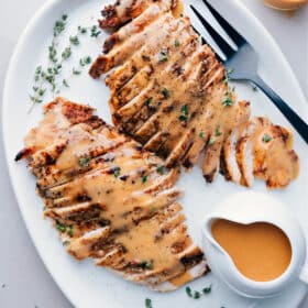 Sliced turkey breast cooked in a crockpot, served on a plate topped with gravy and garnished with fresh herbs.