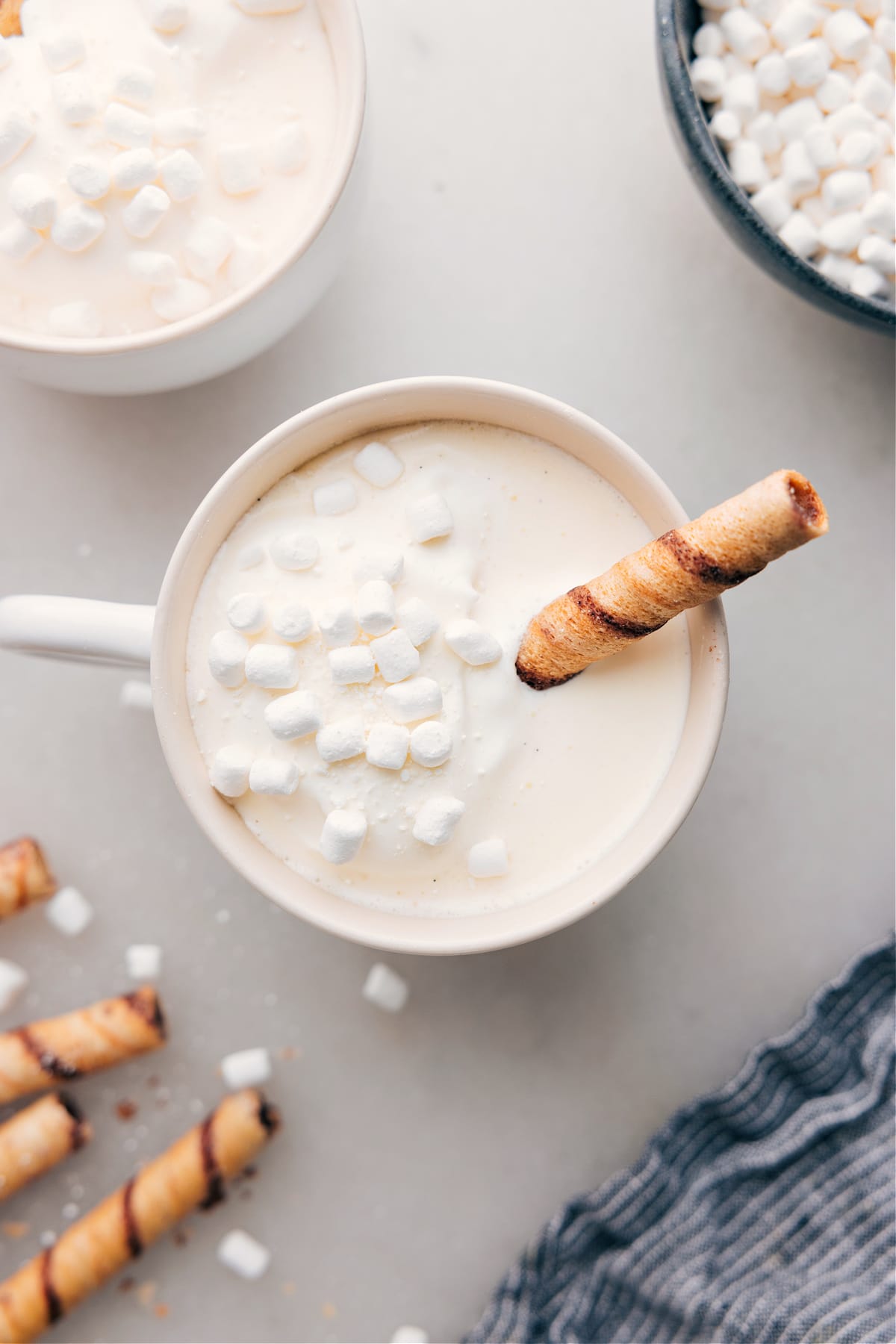 A mug of warm and delicious White Hot Chocolate, with marshmallows floating on top and a chocolate straw coming out of it.