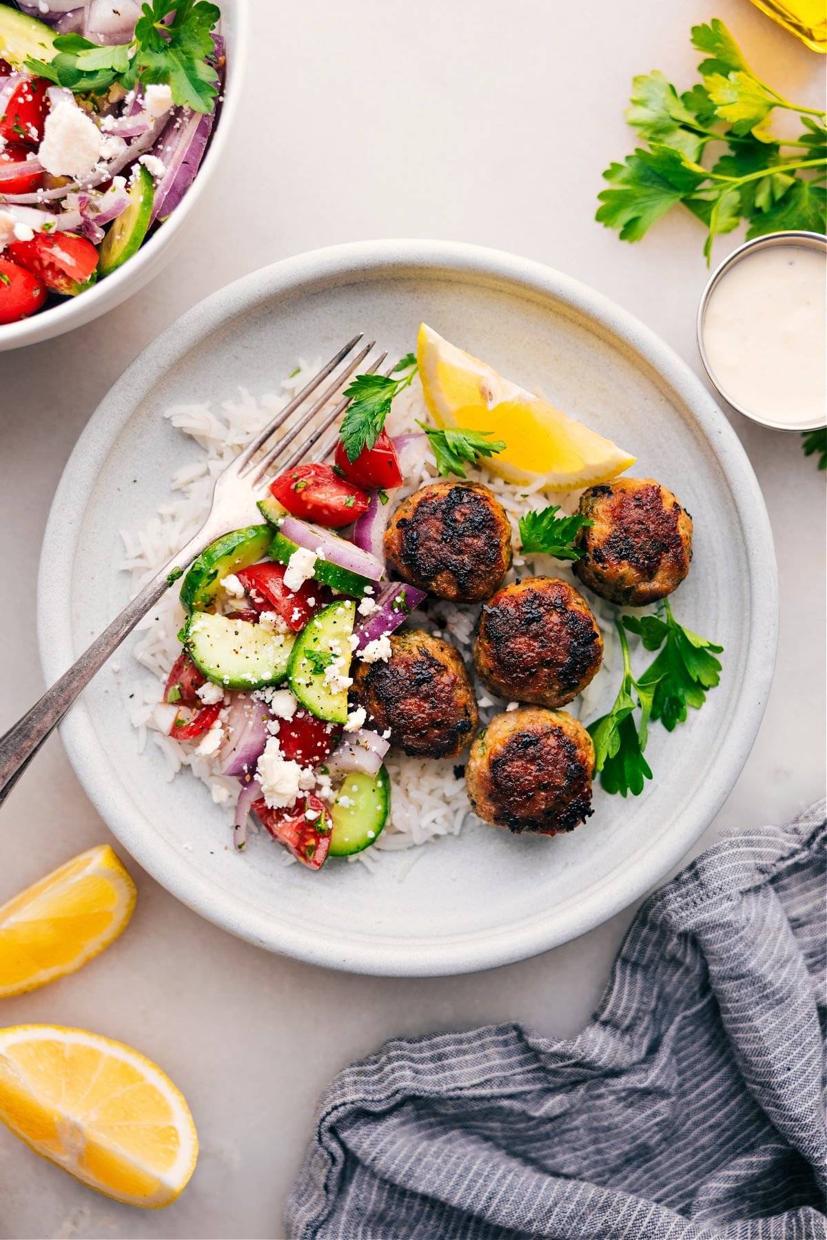 Plate with Greek Turkey Meatballs all over a bed of rice with a cucumber tomato salad on the side.