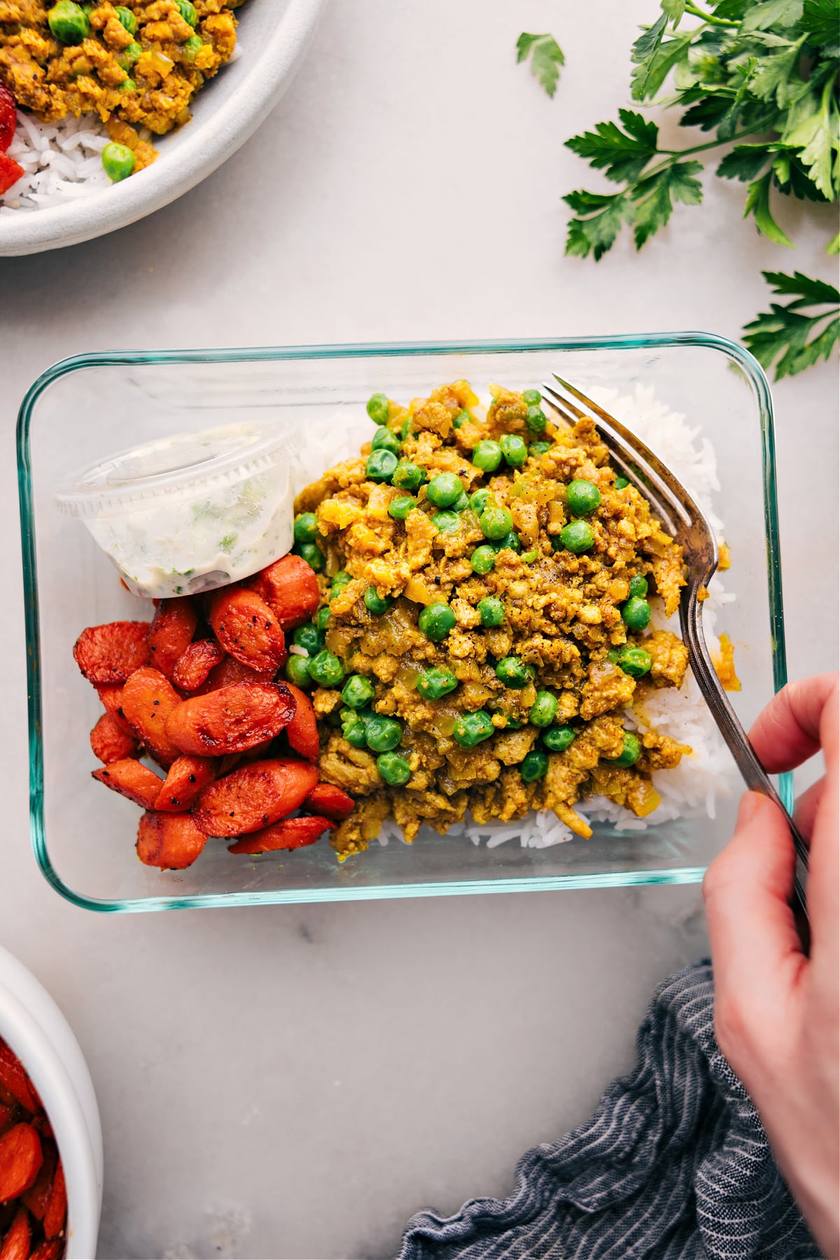 A meal-prepped glass container filled with rice, savory Indian ground turkey, roasted vegetables, and sauce--ready for a quick and delicious meal.