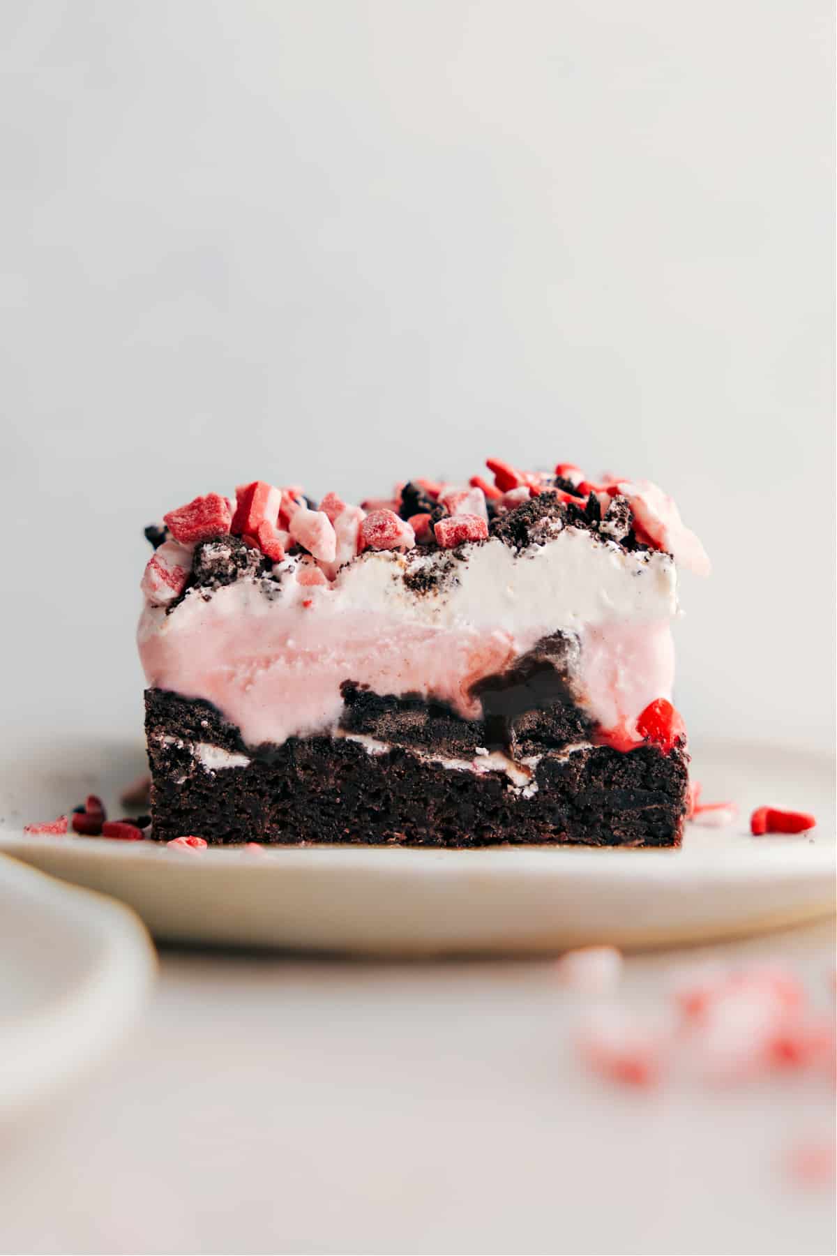 A slice of peppermint brownie ice cream bar, displaying its stunning layers with a rich brownie base, a thick layer of ice cream, and a topping of crushed peppermint, exemplifying a perfect blend of textures and flavors.
