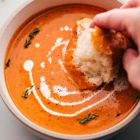 Big bowl of Roasted Red Pepper Soup being dipped with bread.