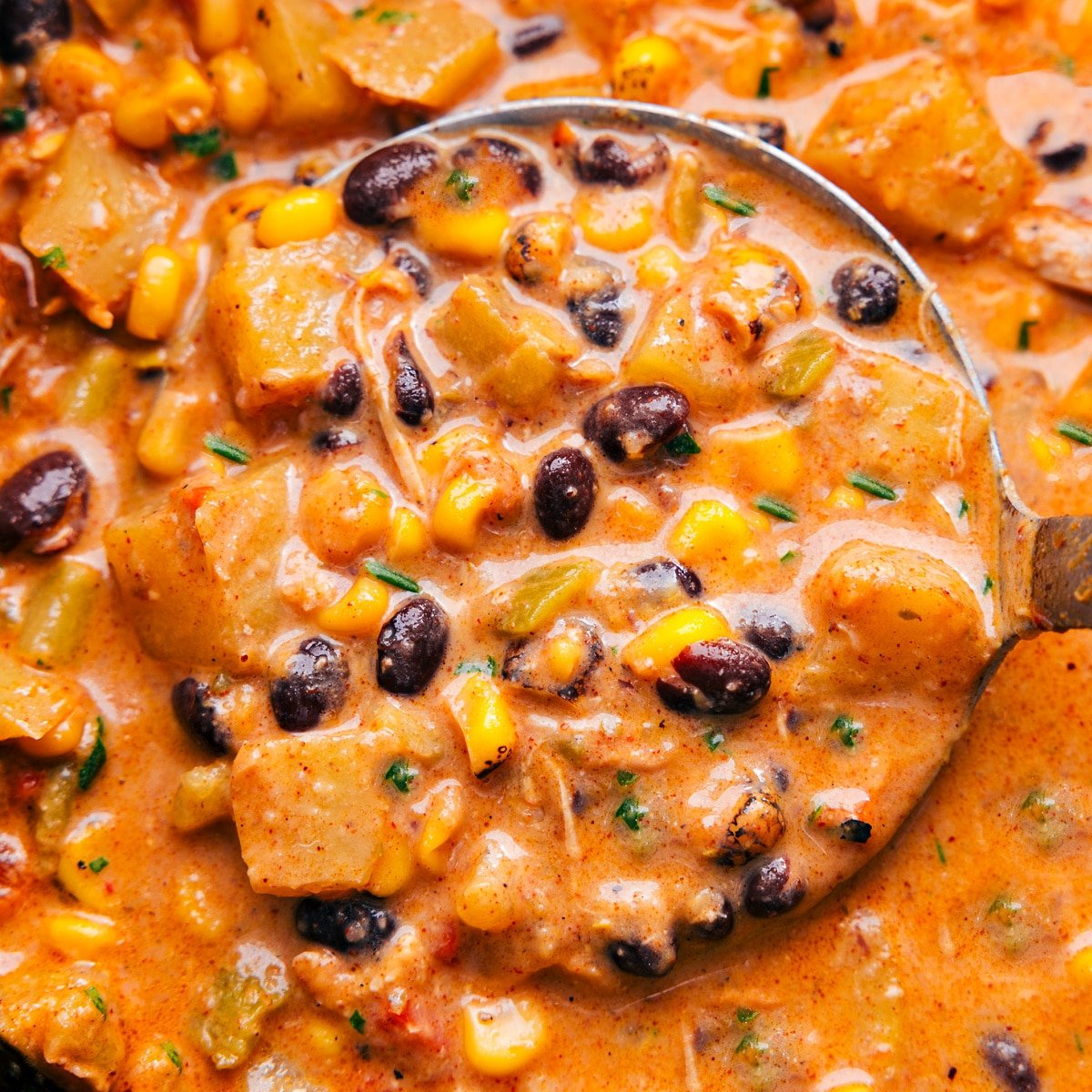 A ladle overflowing with southwestern chicken corn chowder, showcasing its rich and hearty texture, indicating a delicious and comforting meal.