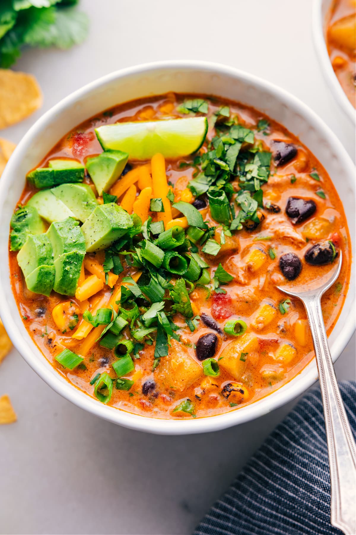 A bowl of the southwestern corn chowder with black beans, generously topped with green onions, melted cheese, and sliced avocados, ready to be enjoyed.