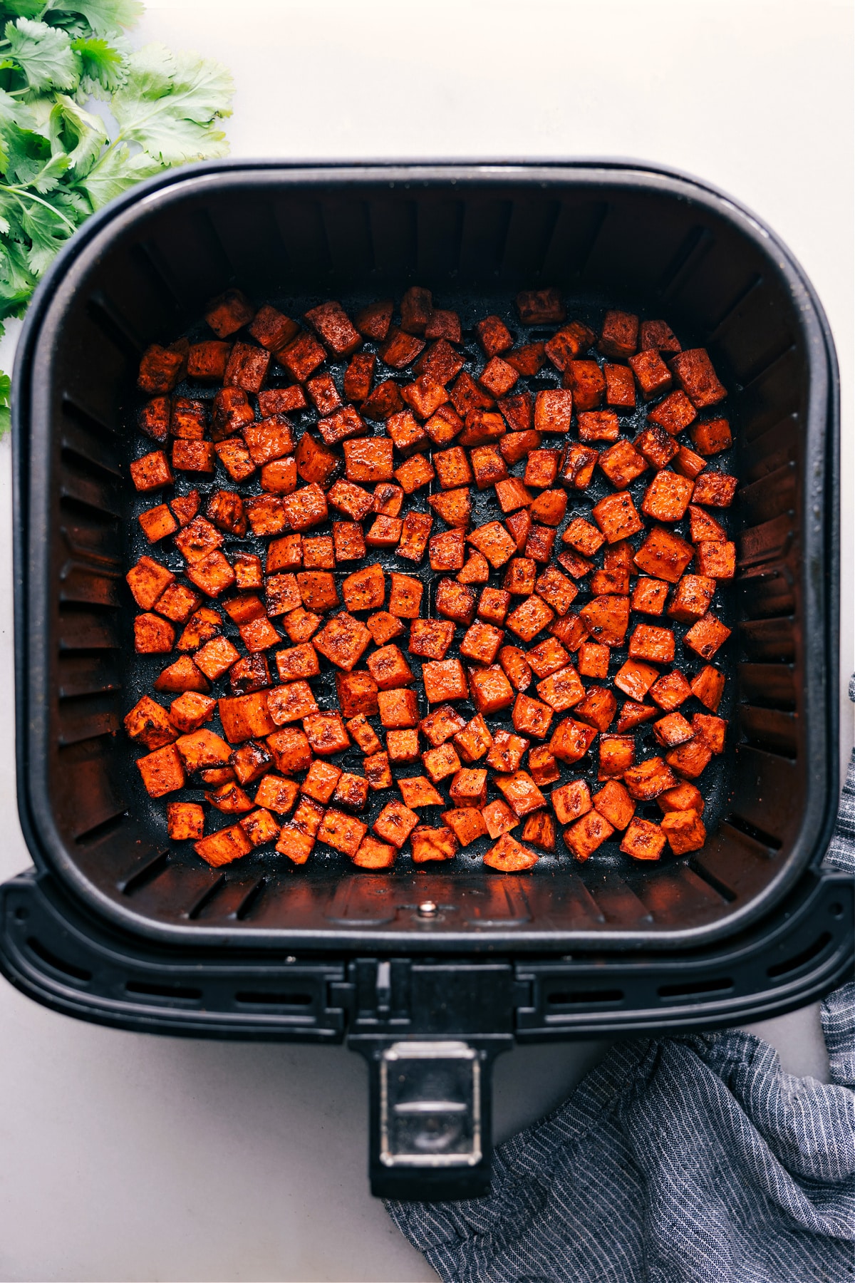 Photo looking down at an air fryer with sweet potato cubes in the basket