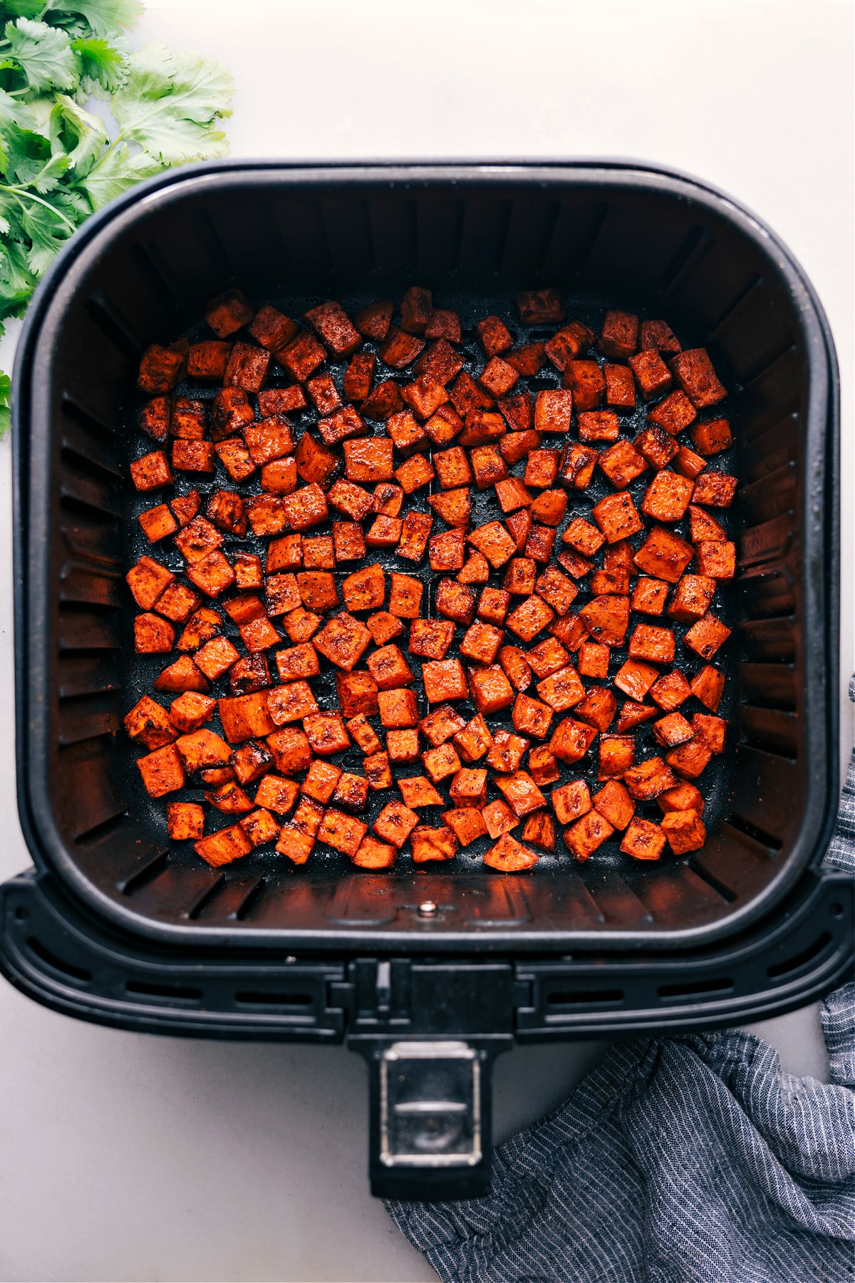 Air Fryer Sweet Potatoes fresh out of the air fryer. Photo looking down at an air fryer with sweet potato cubes in the basket