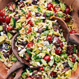Wooden spoons, tossing a batch of Mediterranean Orzo Salad.