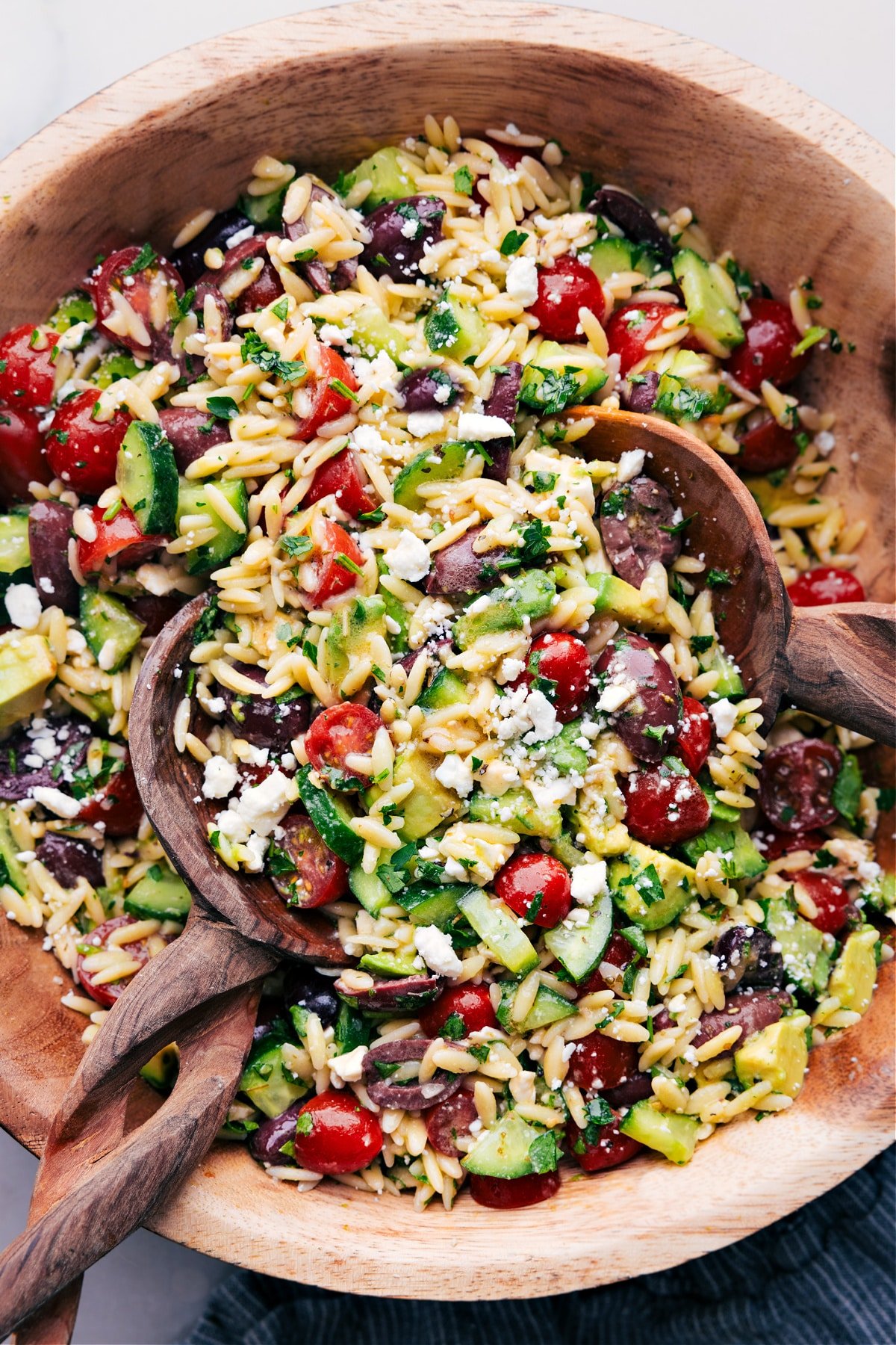 Wooden spoons, tossing a batch of Mediterranean Orzo Salad.