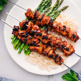 Baked Chicken Bites on skewers over rice and asparagus.