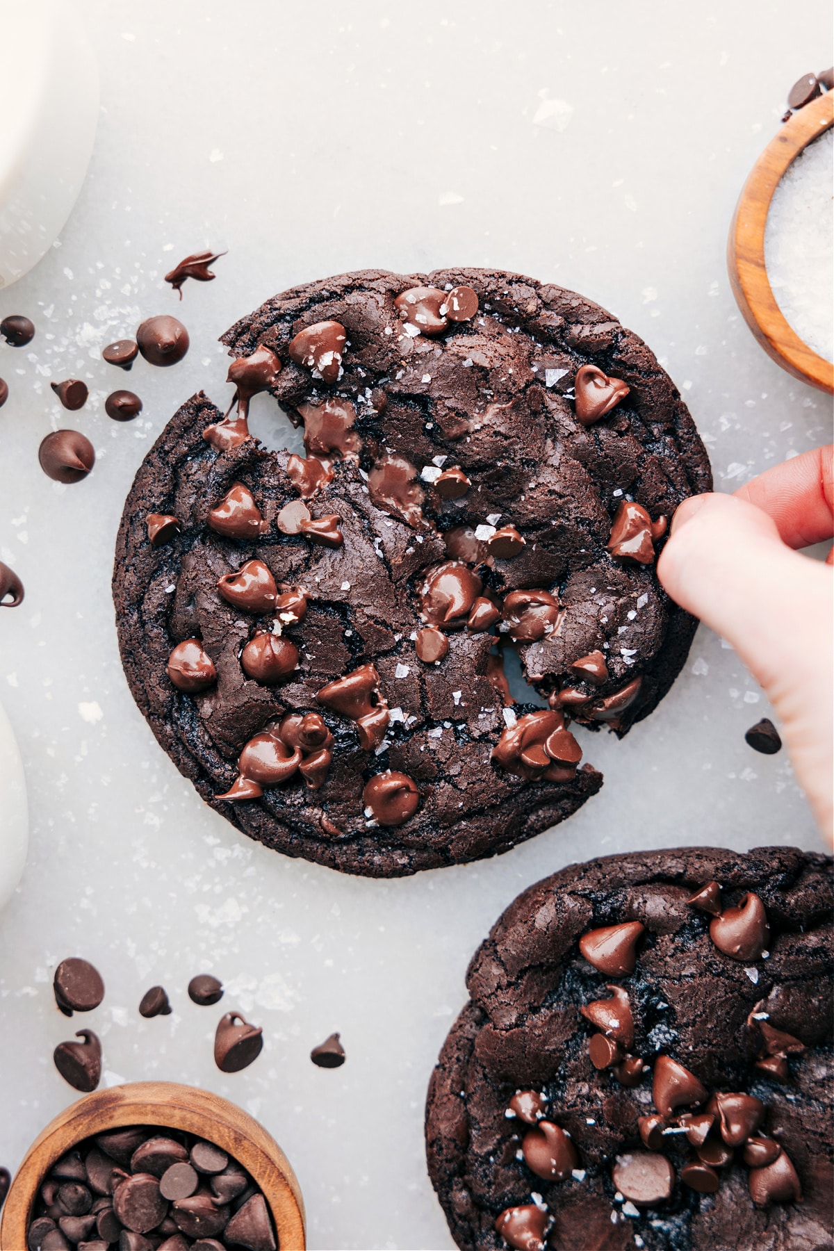 Single serve double chocolate chip cookie with flaky sea salt and a hand breaking it open.