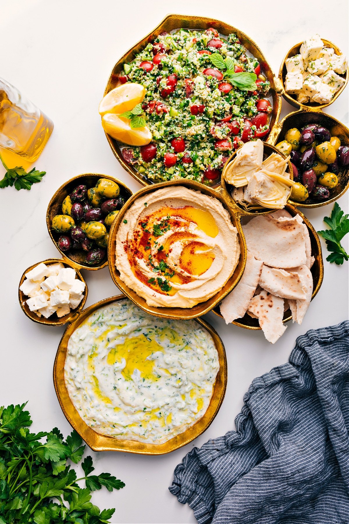 A gold serving platter filled with dips, salad, and cheeses.