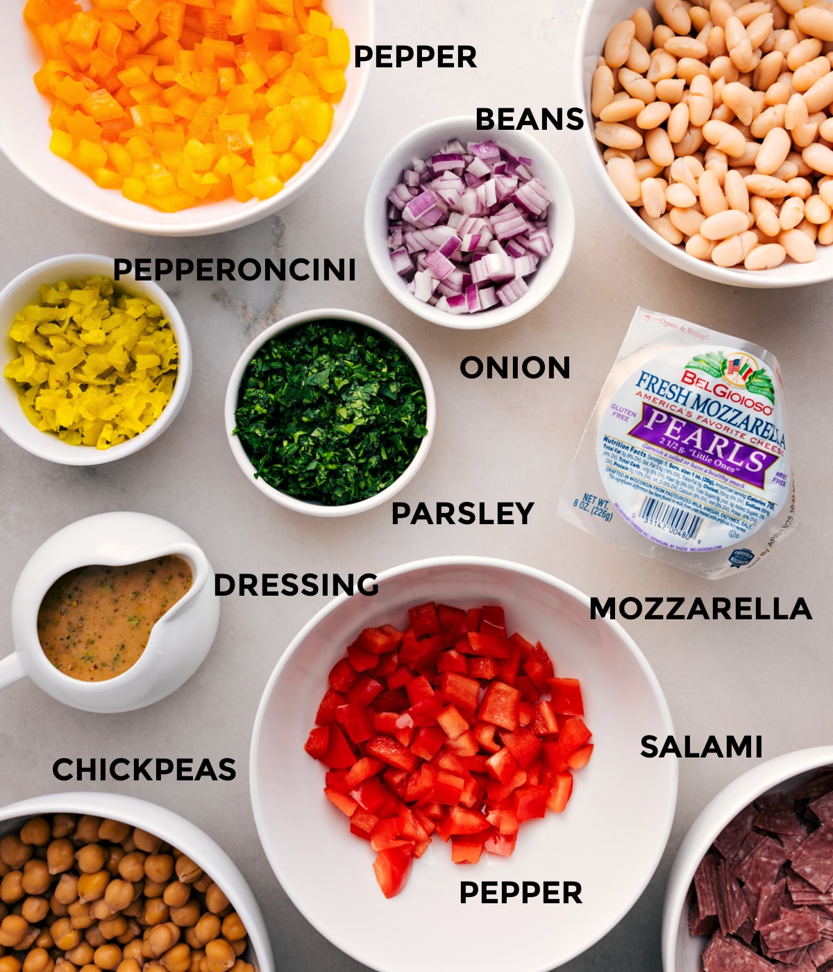 All the ingredients for this recipe are prepped and ready for easy assembly: beans, onion, parsley, mozzarella, pepper salami, pepperoncini, chickpeas, and dressing.