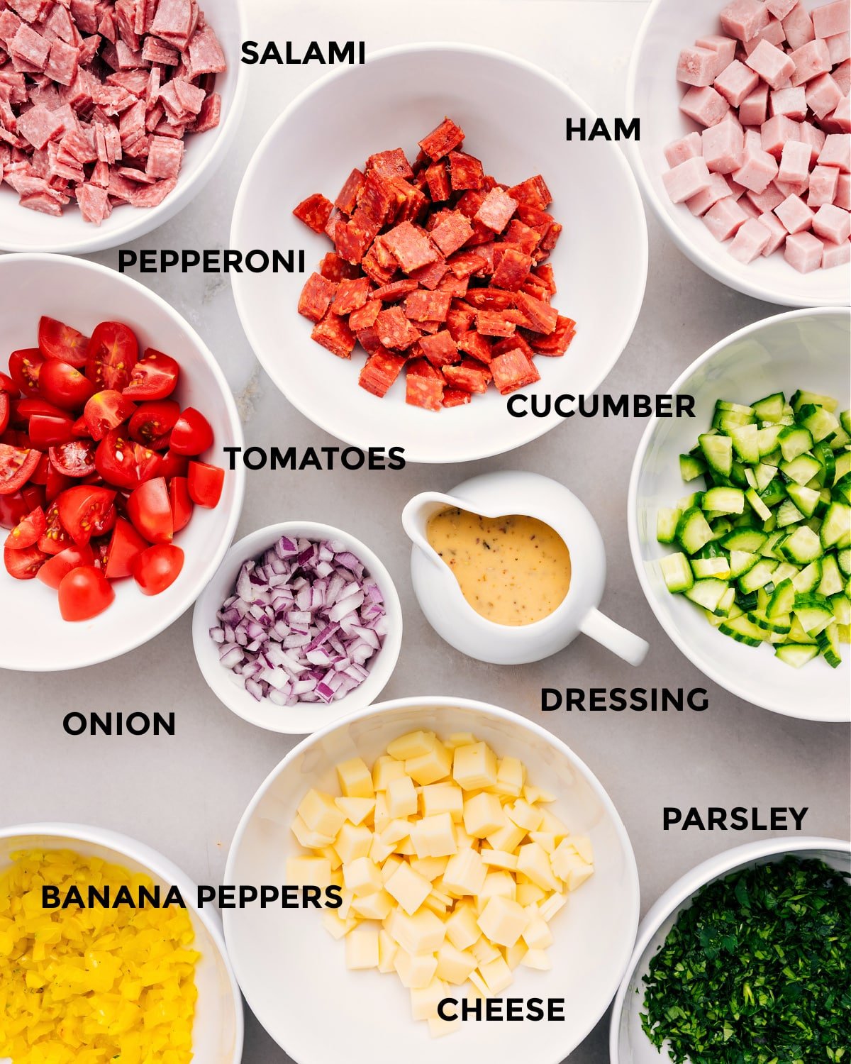 All the ingredients are prepped for easy assembly—meat, cucumber, tomatoes, onion, dressing, cheese, banana peppers, and parsley.