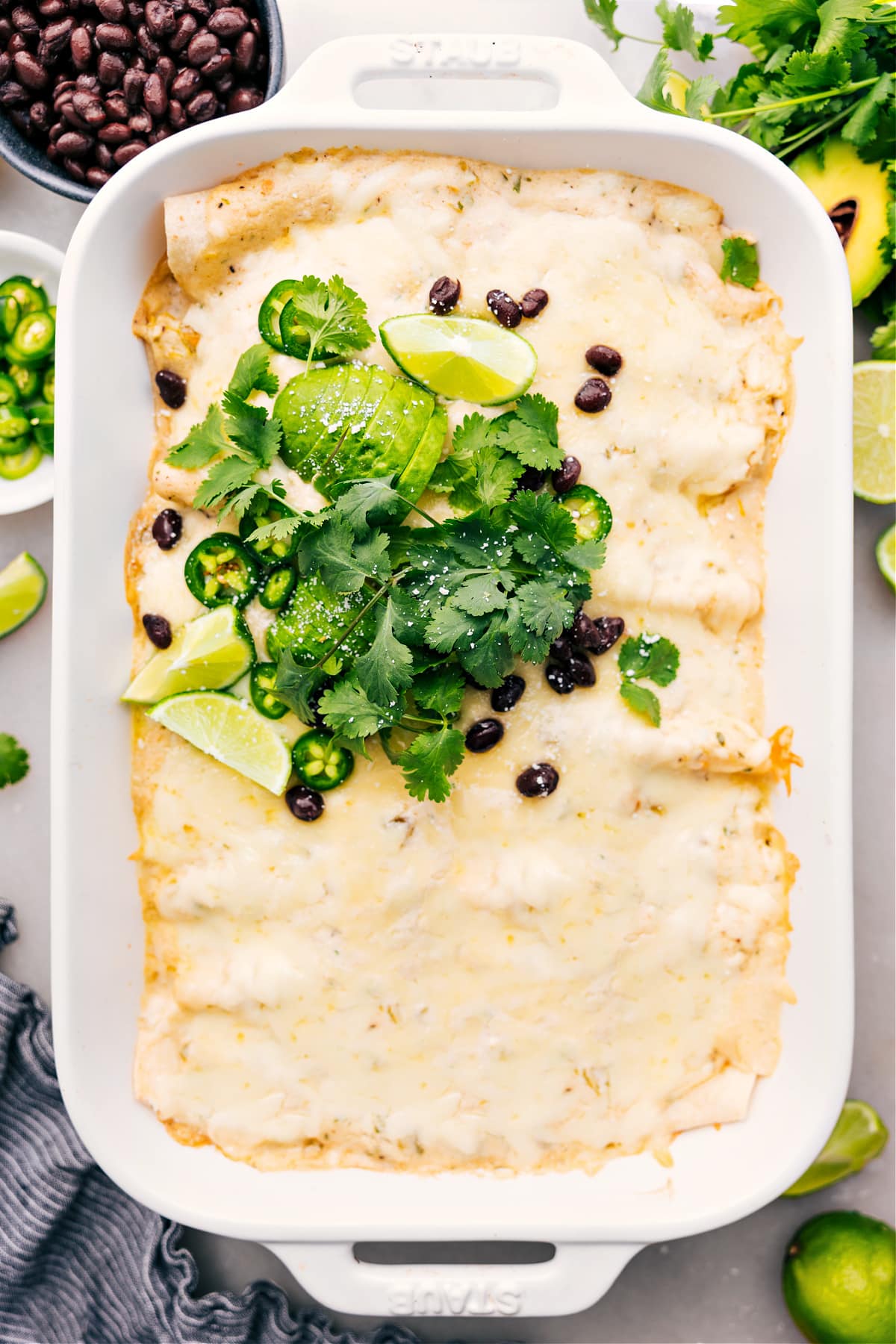 The Best White Chicken Enchiladas White Chicken Enchiladas in the casserole dish, topped with fresh cilantro, sliced jalapeños, lime wedges, and crumbled cotija.