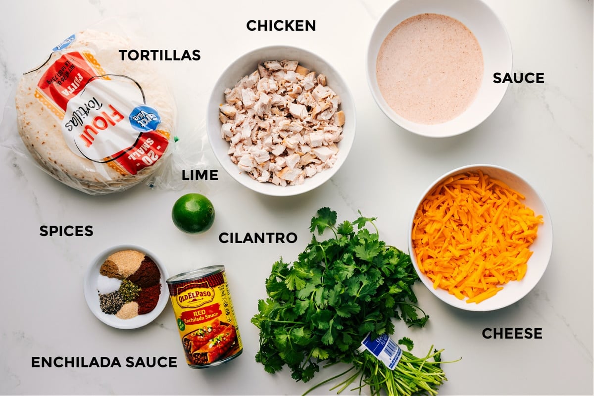All the ingredients for this recipe prepped and ready for easy assembly, including chicken, sauce, cheese, cilantro, enchilada sauce, spices, tortillas, and limes.