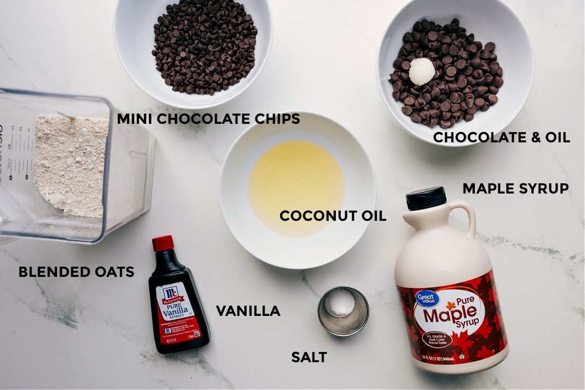 All the ingredients for this recipe are prepped and ready for easy assembly, including chocolate, coconut oil, maple syrup, vanilla, salt, and oats.