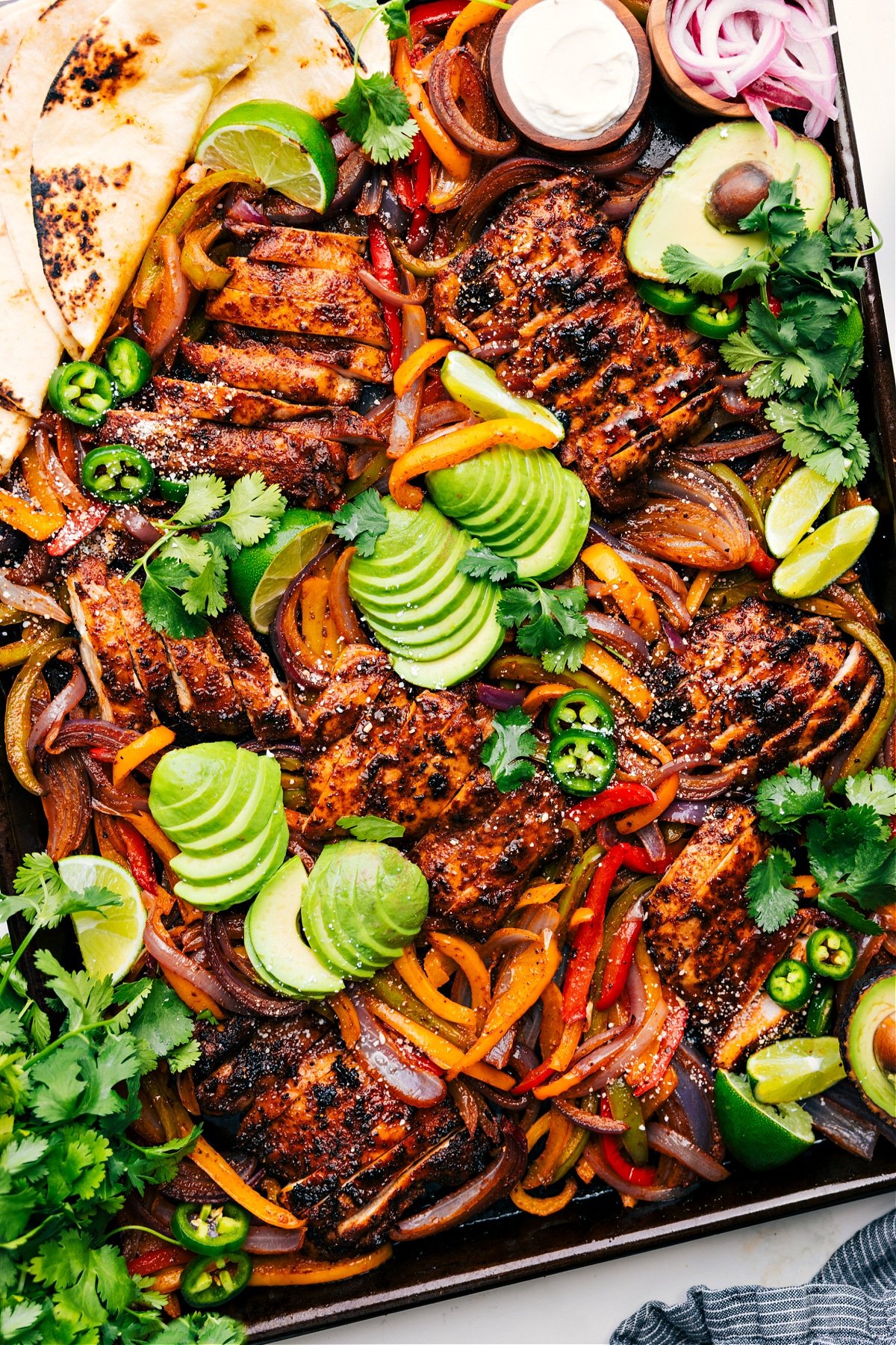 Make An Entire Chicken Fajita Dinner On One Sheet Pan Sheet Pan Chicken Fajitas on the pan topped with fresh avocado, jalapeños, and cilantro.