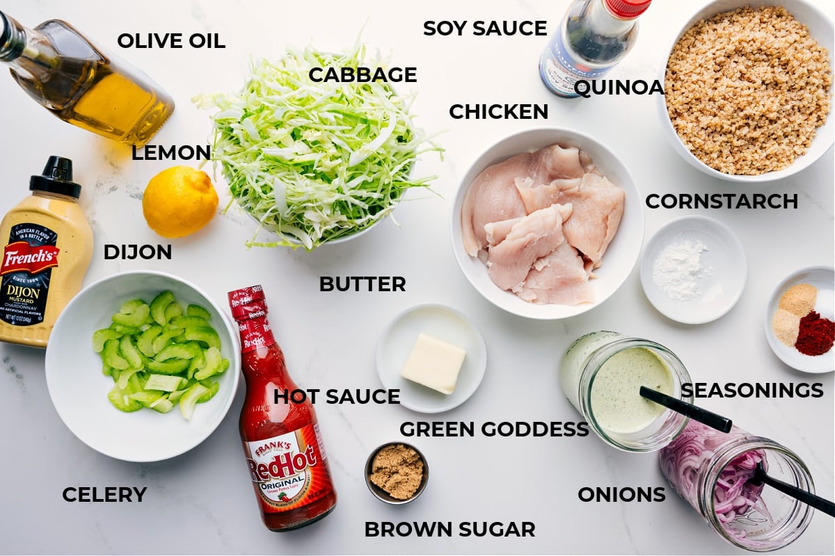 All the ingredients prepped for easy assembly, including olive oil, cabbage, chicken, soy sauce, quinoa, cornstarch, seasonings, dressing, onions, butter, hot sauce, celery, Dijon, and lemon.