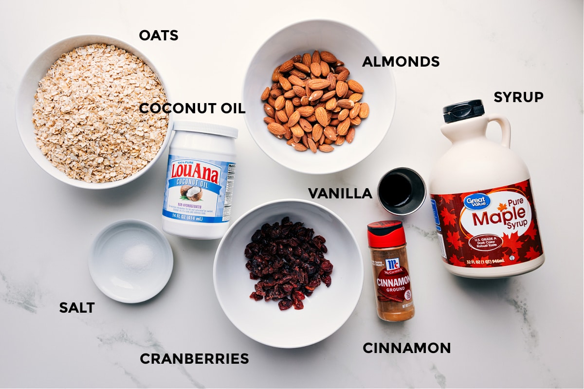 Ingredients in recipe prepped out for easy assembly including the coconut oil, oats, almonds, vanilla, syrup, cinnamon, cranberries, and salt.
