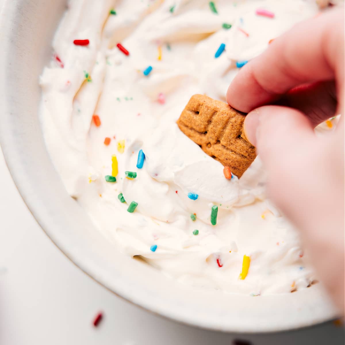 Funfetti-flavored fluffy yogurt in a bowl with a graham cracker dipped into it.