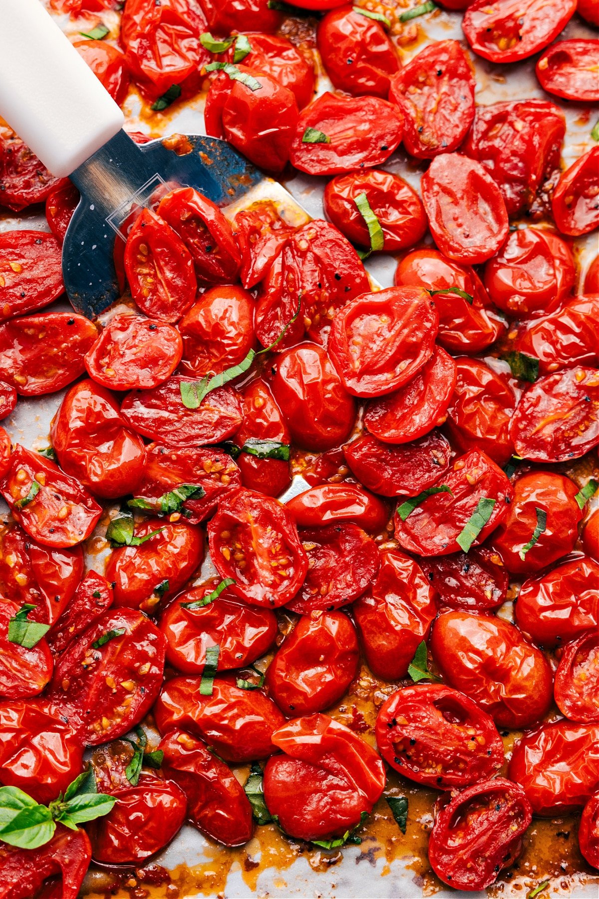 Roasted Cherry Tomatoes on a sheet pan with a spatula lifting a portion.