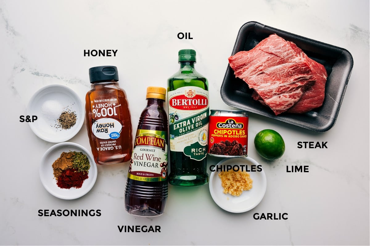Marinade ingredients laid out for steak including spices, honey, vinegar, oil, chipotles, lime, and garlic.