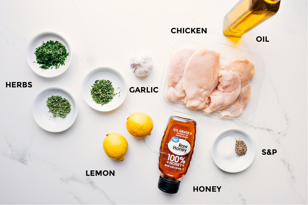 All the ingredients in this recipe prepped out for easy assembly including the herbs, lemon, garlic, chicken, honey, and oil.