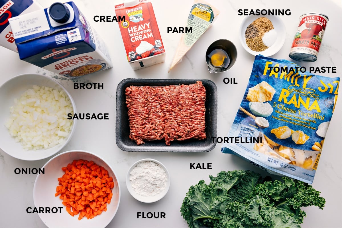 All the ingredients prepped for easy assembly, including broth, sausage, onion, carrot, cream, flour, Parmesan, oil, tortellini, kale, seasonings, and tomato paste.