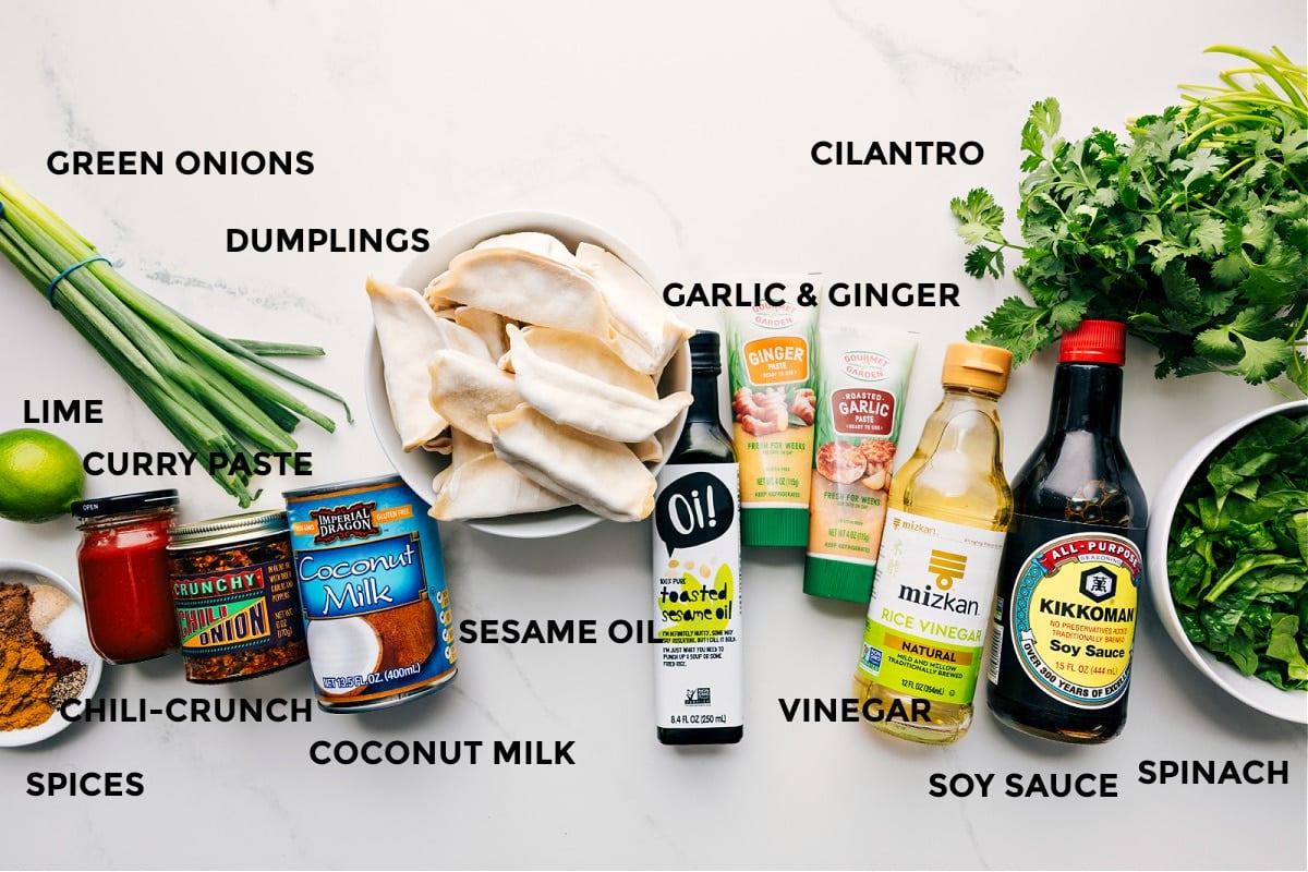 All the ingredients prepped for easy assembly including spices, lime, green onions, dumplings, chili crunch, curry paste, sesame oil, garlic, ginger, cilantro, vinegar, soy sauce, and spinach.