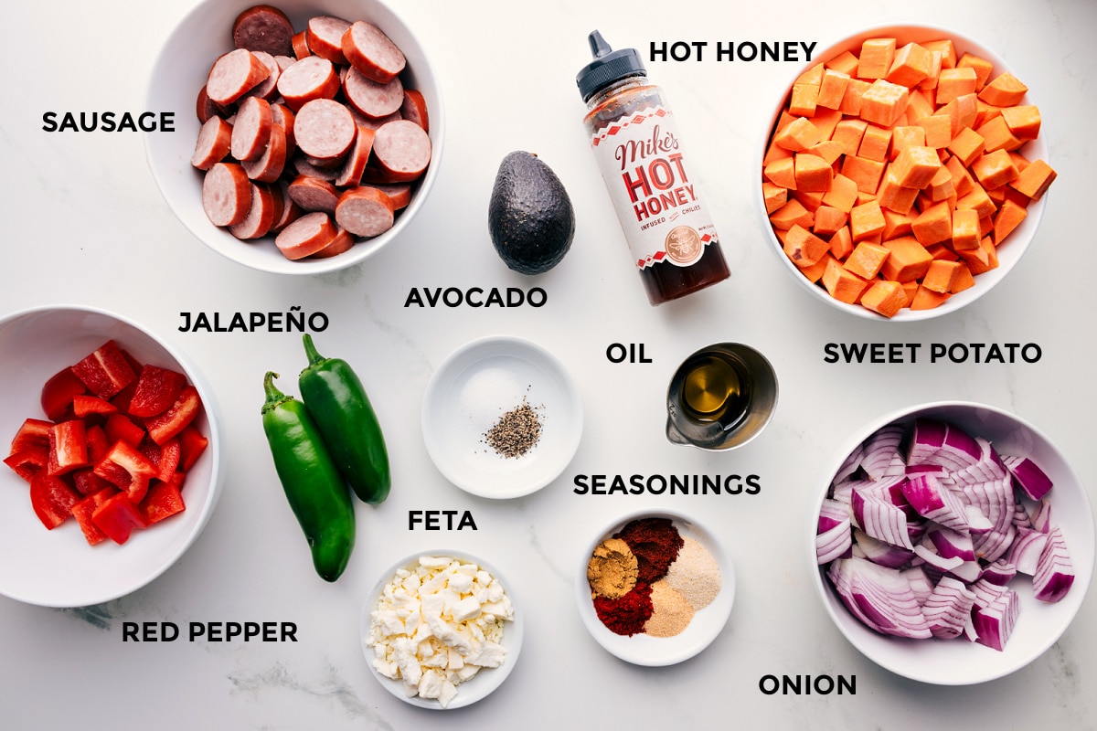 Ingredients In Sheet Pan Hot Honey Sausage & Veggies All the ingredients in this recipe prepped out for easy assembly including the red pepper, sausage, jalapeño, feta, avocado, seasonings, oil, hot honey, onion, and sweet potatoes.