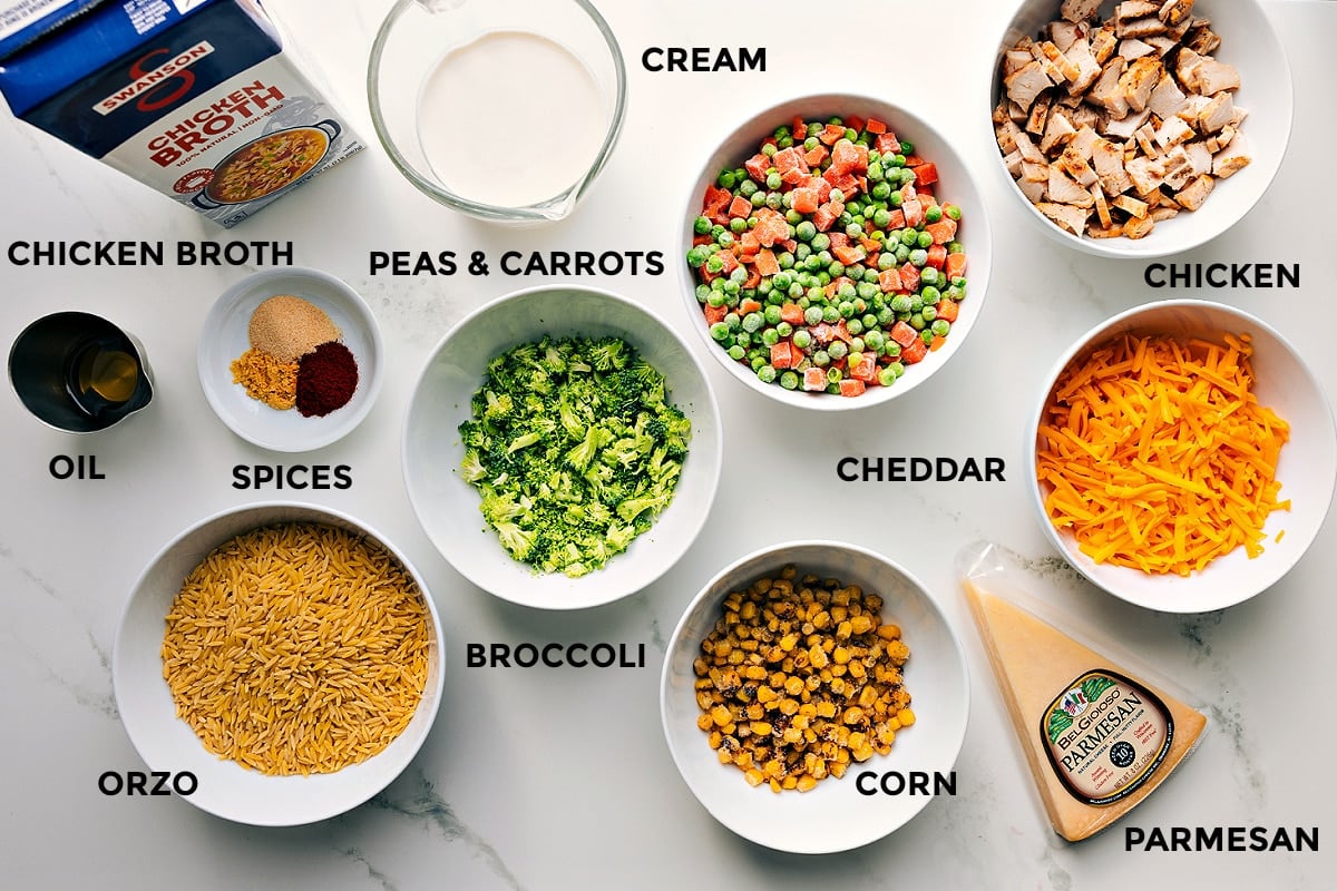 Ingredients In Chicken Orzo Bake Ingredients prepped and arranged for easy assembly, including broth, cream, oil, spices, vegetables, chicken, cheddar, parmesan, corn, and orzo.