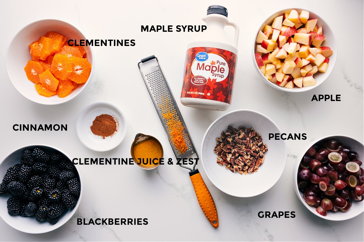 All the ingredients for Fall Fruit Salad prepped for easy assembly, including clementines, blackberries, grapes, apples, pecans, cinnamon, orange juice and zest, and maple syrup.