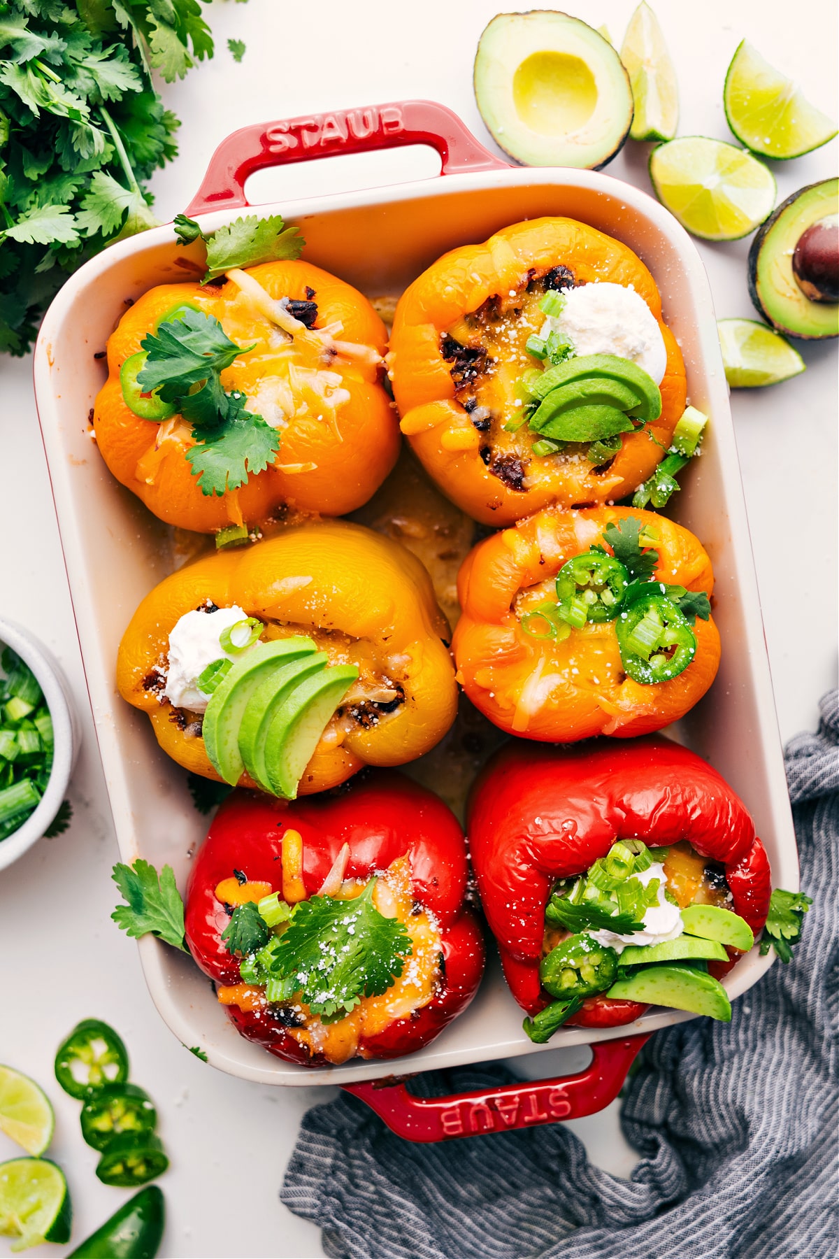 Mexican stuffed peppers in a pan topped with fresh cilantro, sliced jalapeños, sour cream, and avocado pieces.
