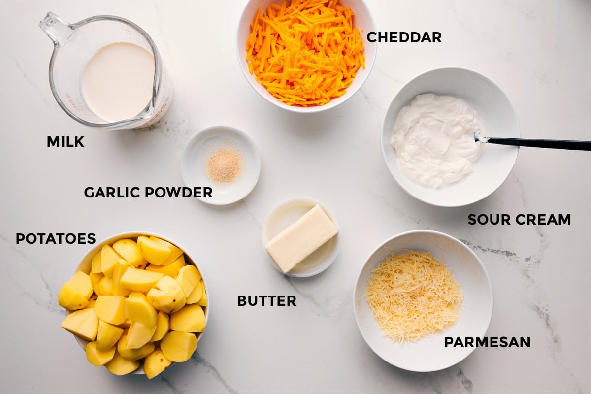 All the ingredients in this recipe prepped out for easy assembly including the milk, garlic powder, potatoes, butter, parmesan, sour cream, and cheddar.