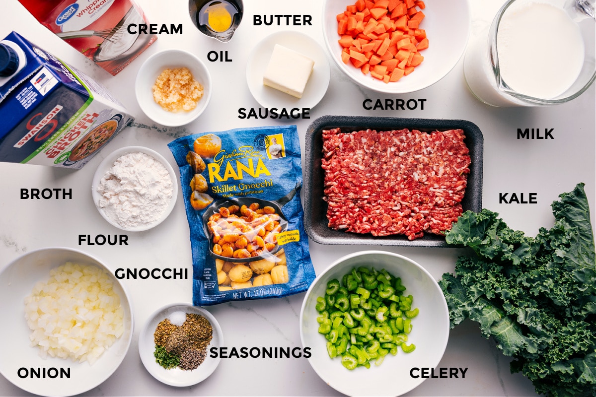 All the ingredients in this recipe prepped out for easy assembly including the broth, cream, flour, onion, gnocchi, seasonings, celery, kale, milk, carrot, sausage, butter, and oil.