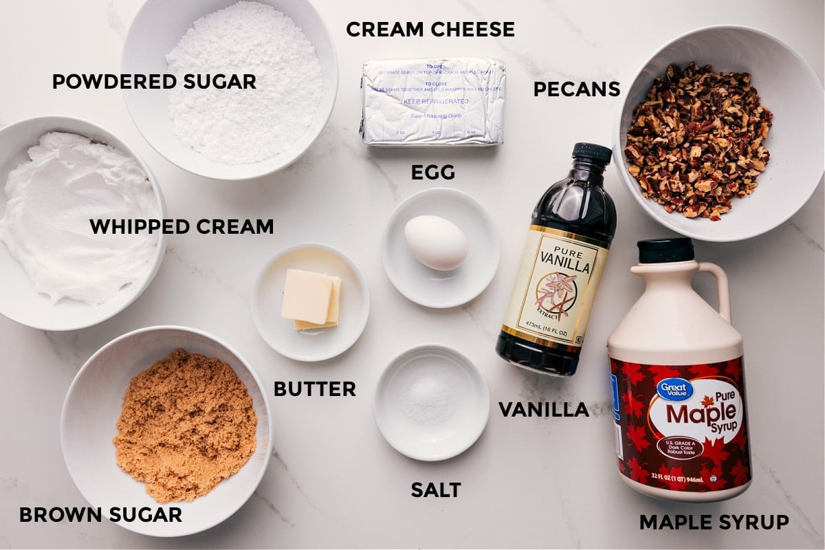Ingredients In Pecan Pie Dip Recipe All the ingredients in pecan pie dip laid out for easy assembly including the whipped cream, brown sugar, butter, powdered sugar, egg, cream cheese, salt, vanilla, pecans, and maple syrup.