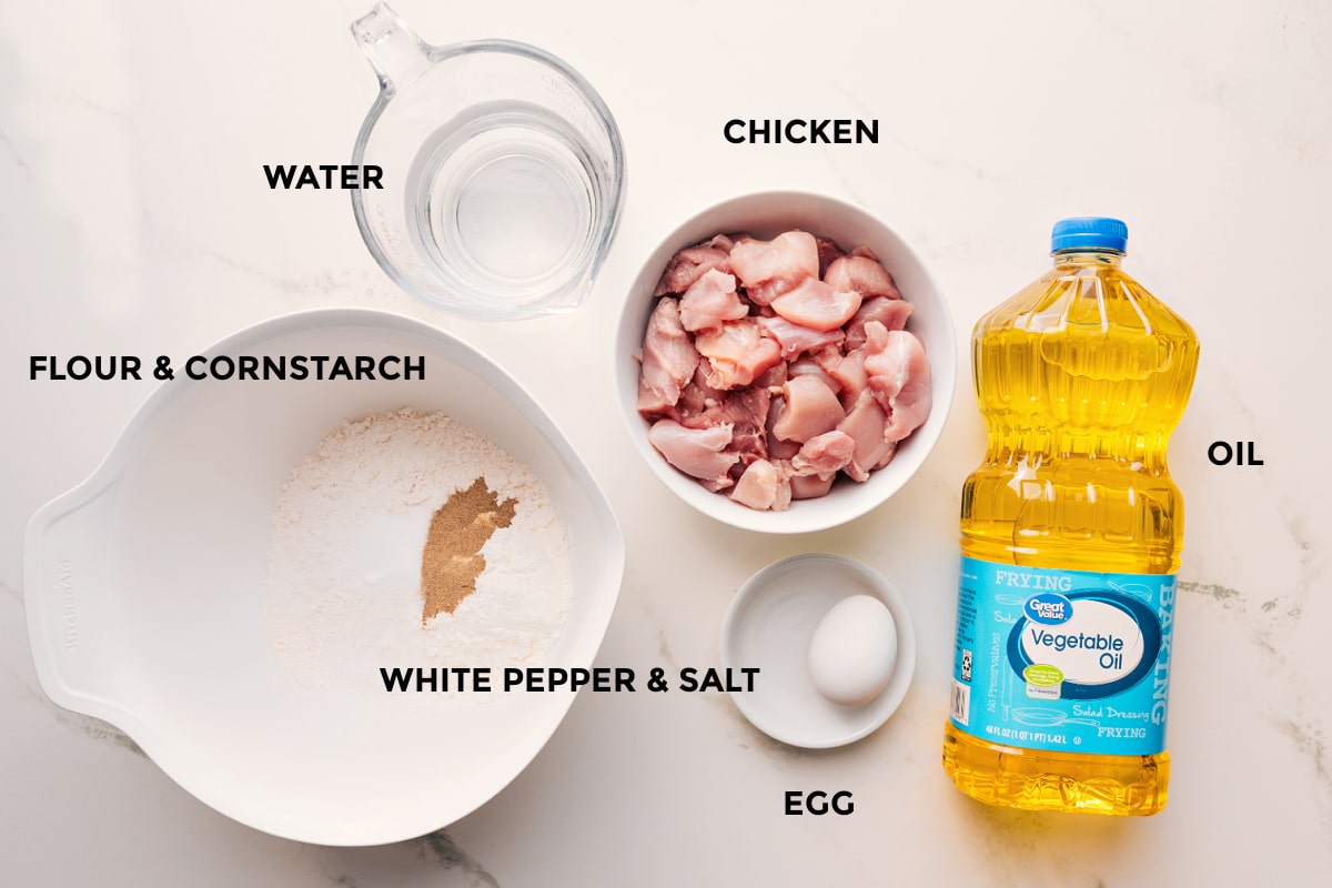 Korean chicken recipe ingredients prepped out for easy assembly including the flour, cornstarch, water, chicken, white pepper, salt, egg, and oil.