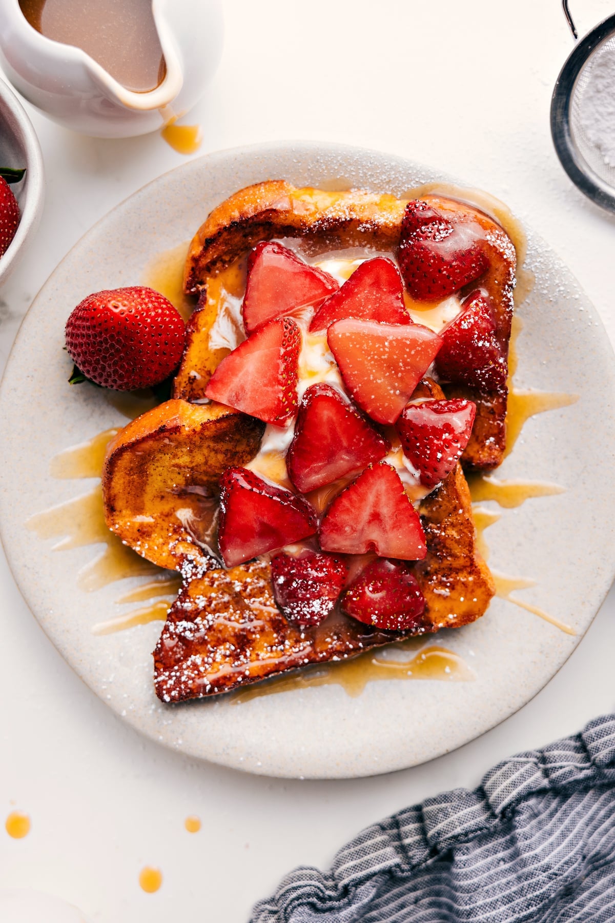 French Toast Recipe topped with fresh whipped cream, sliced strawberries, and maple syrup.