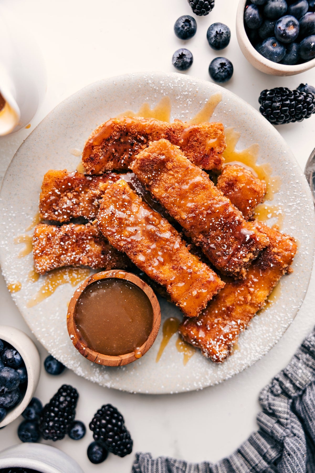 Cinnamon-Sugar French Toast Sticks French Toast Sticks Recipe served on a plate with maple syrup and powdered sugar.