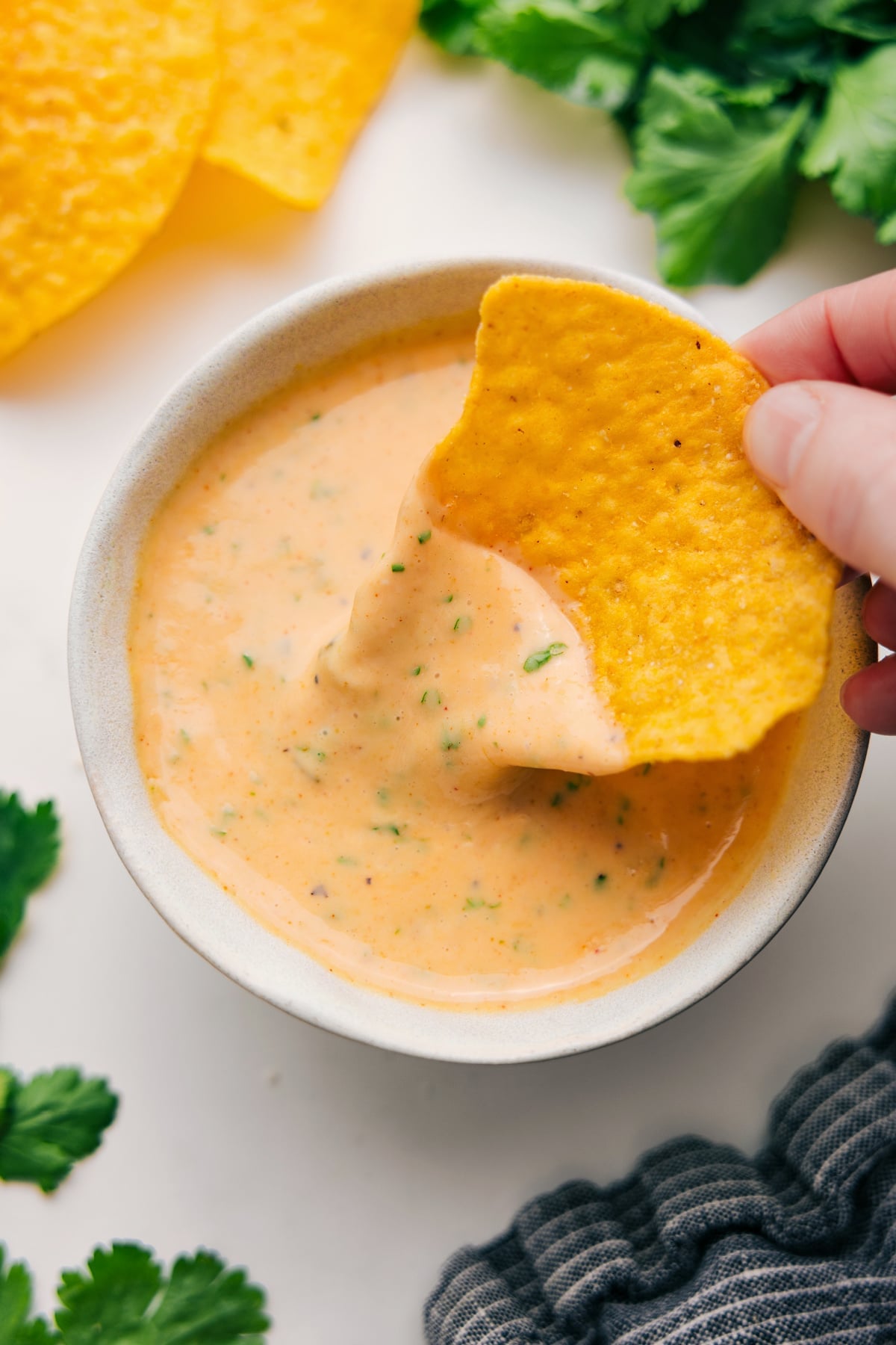 Smooth and Melty Queso Dip Queso dip in a bowl with a tortilla chip dipping into the melted cheese.