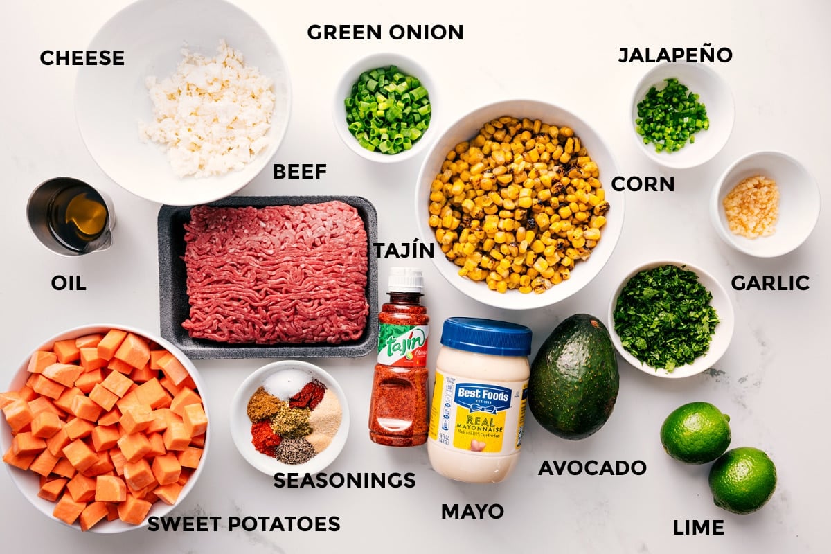 Ingredients In Street Corn Beef Bowl All the ingredients in this recipe prepped out for easy assembly including the cheese, oil, sweet potatoes, beef, seasonings, tajin, mayo, avocado, lime, garlic, jalapeno, corn, and green onions.
